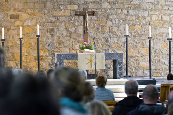 Gemeindegottesdienst in einer Kirche; im Vordergrund sitzt die versammelte Gemeinde, im Hintergrund stehen Altar, Kreuz und Kerzen vor einer Natursteinwand.